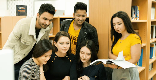 A group of BPP Institute students crowd around a desk with textbooks in a campus library